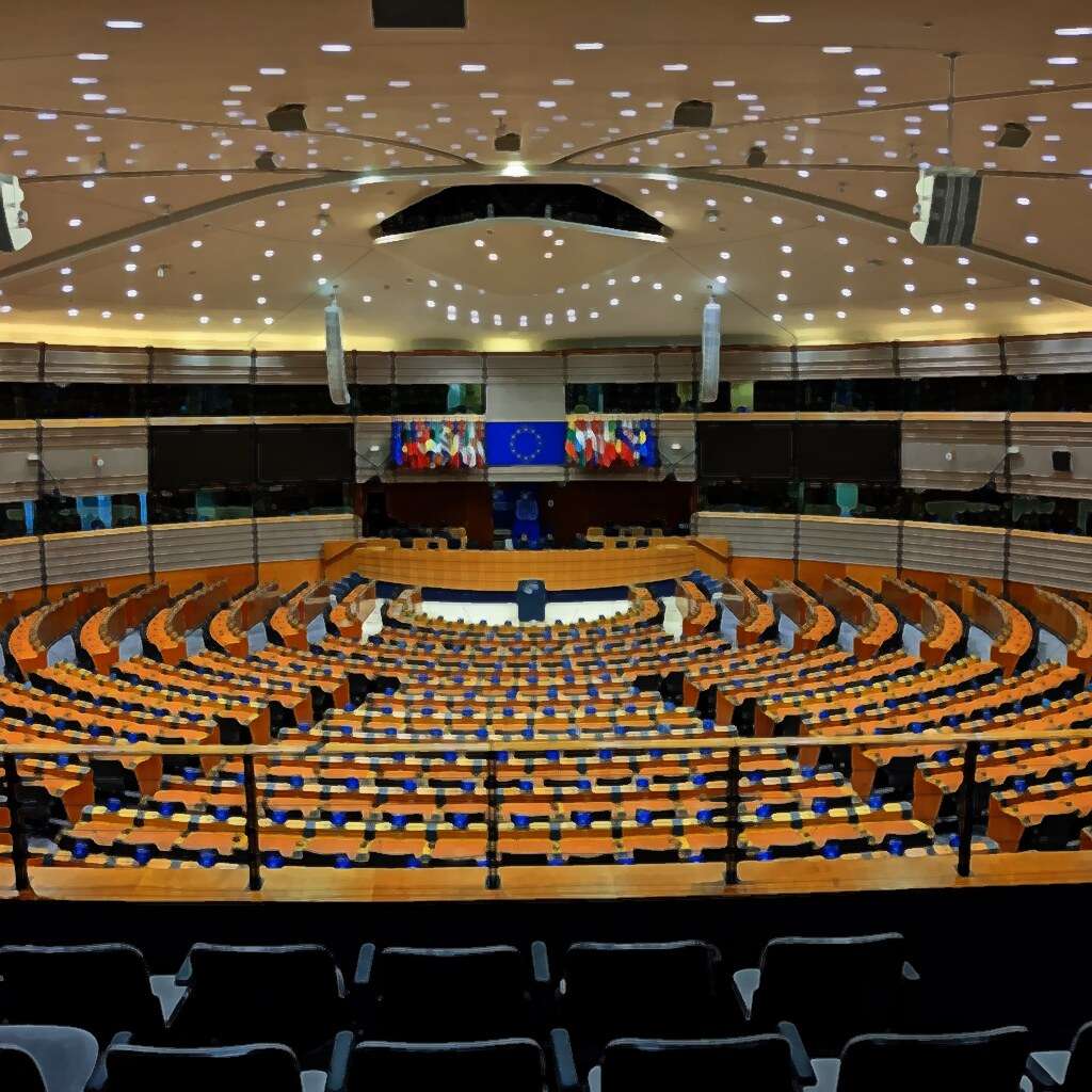 The hemicycle of the European Parliament in Brussels, with the EU flag and the flags of the member states behind the podium